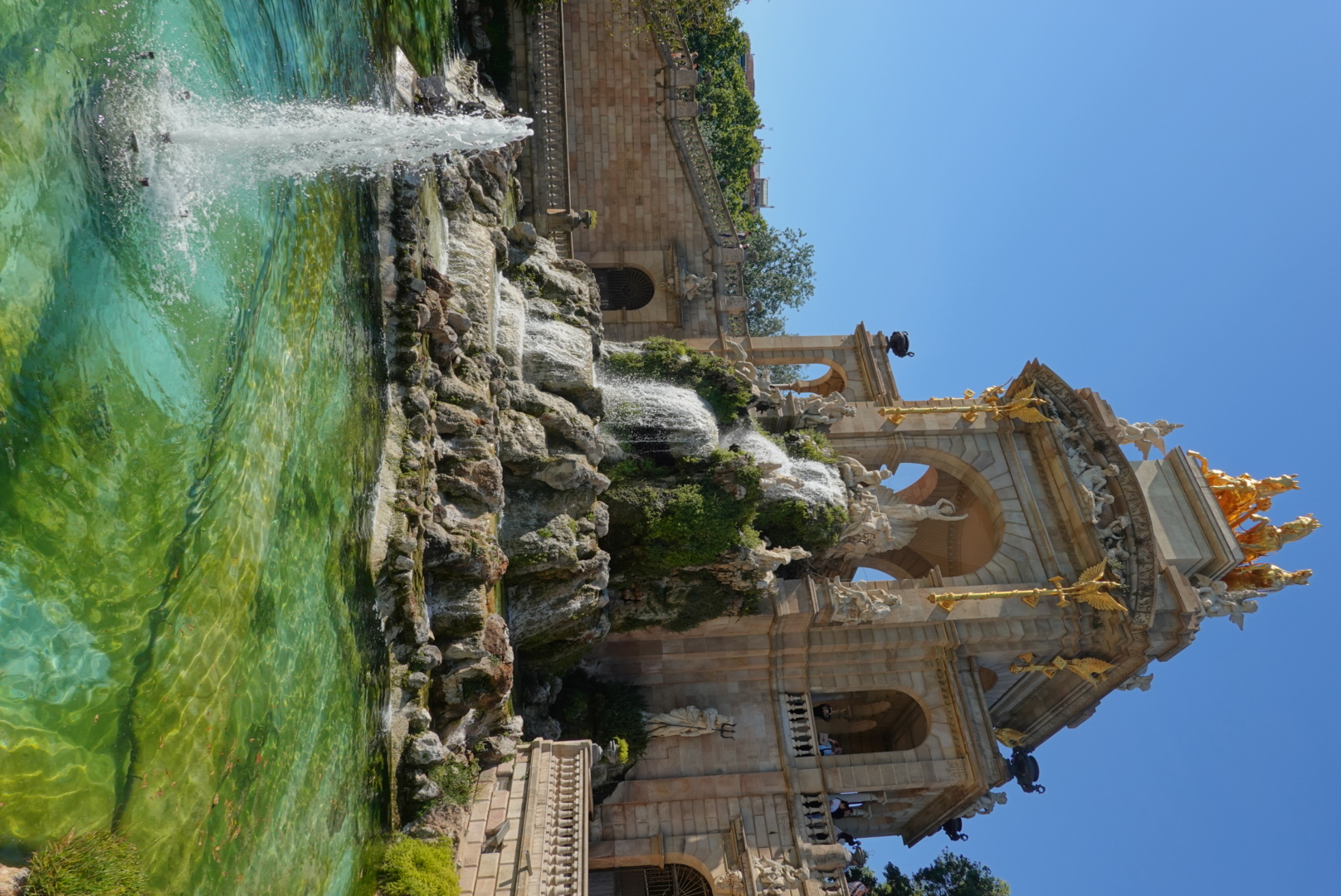 Gold-topped Cascada monumental fountain cascading over mossy rocks into a turquoise pool in Parc de la Ciutadella