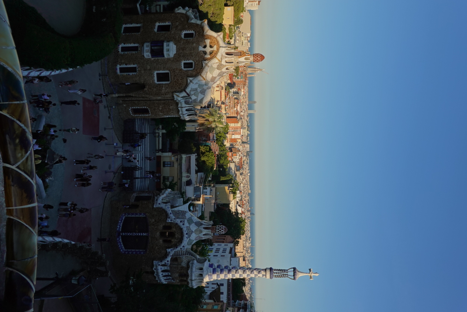Gaudí's mosaic-topped gingerbread pavilions at the Park Güell entrance with Barcelona and the Mediterranean stretching to the horizon at golden hour