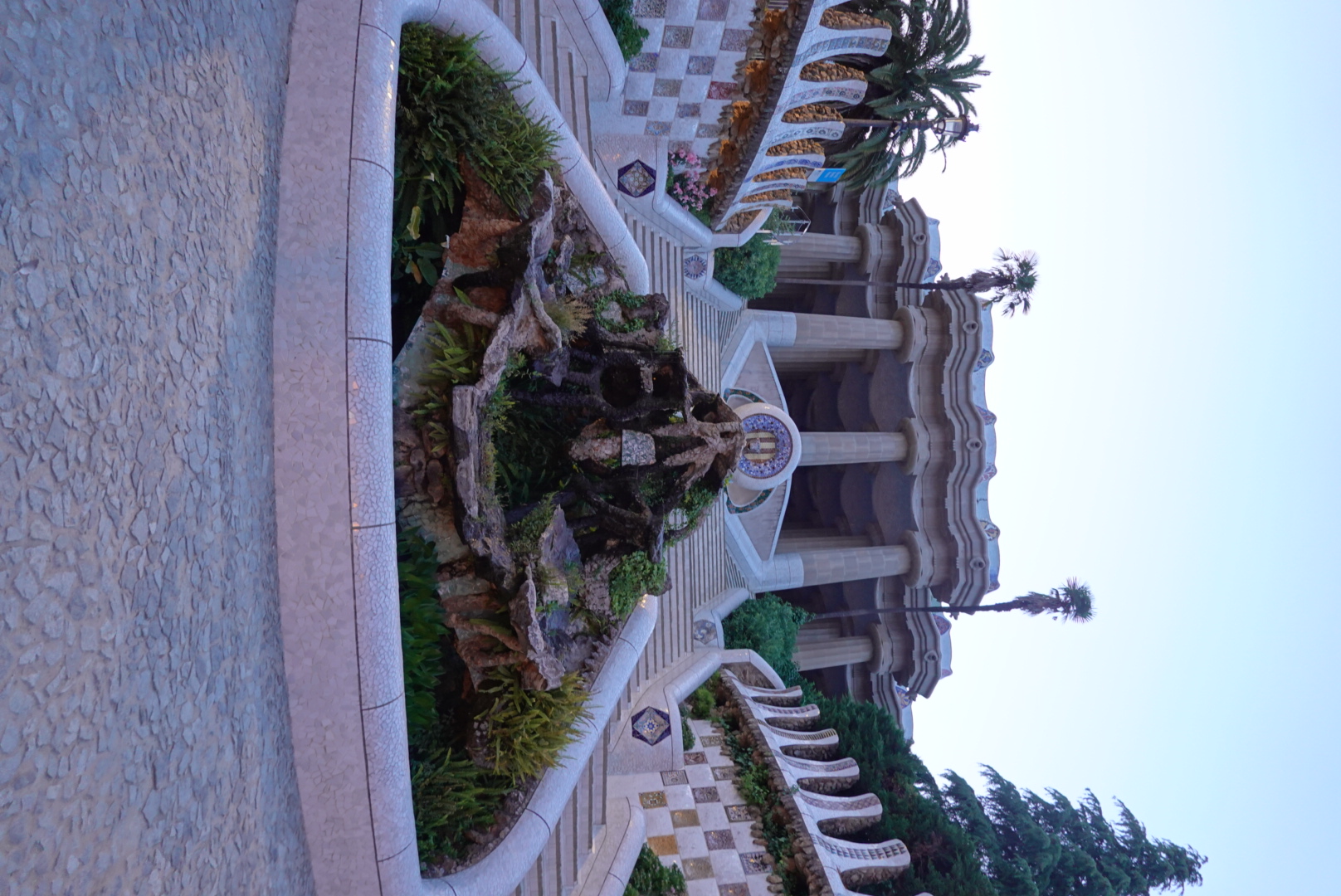 Park Güell's symmetrical main staircase with dragon fountain and mosaic balustrades leading up to the Hypostyle Room at dusk