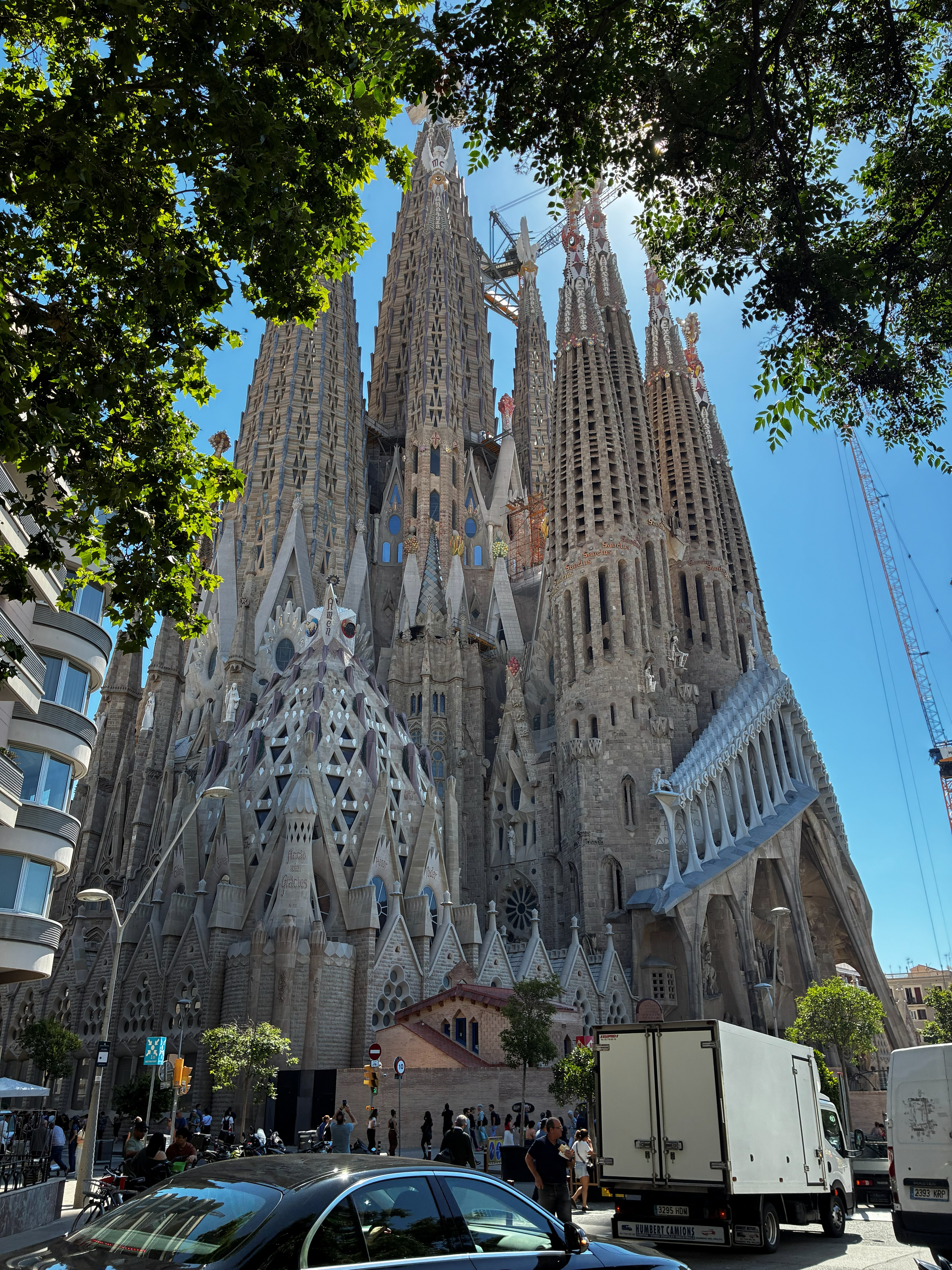 Close-up street-level view of La Sagrada Família's intricate Nativity facade with cranes overhead on a sunny day