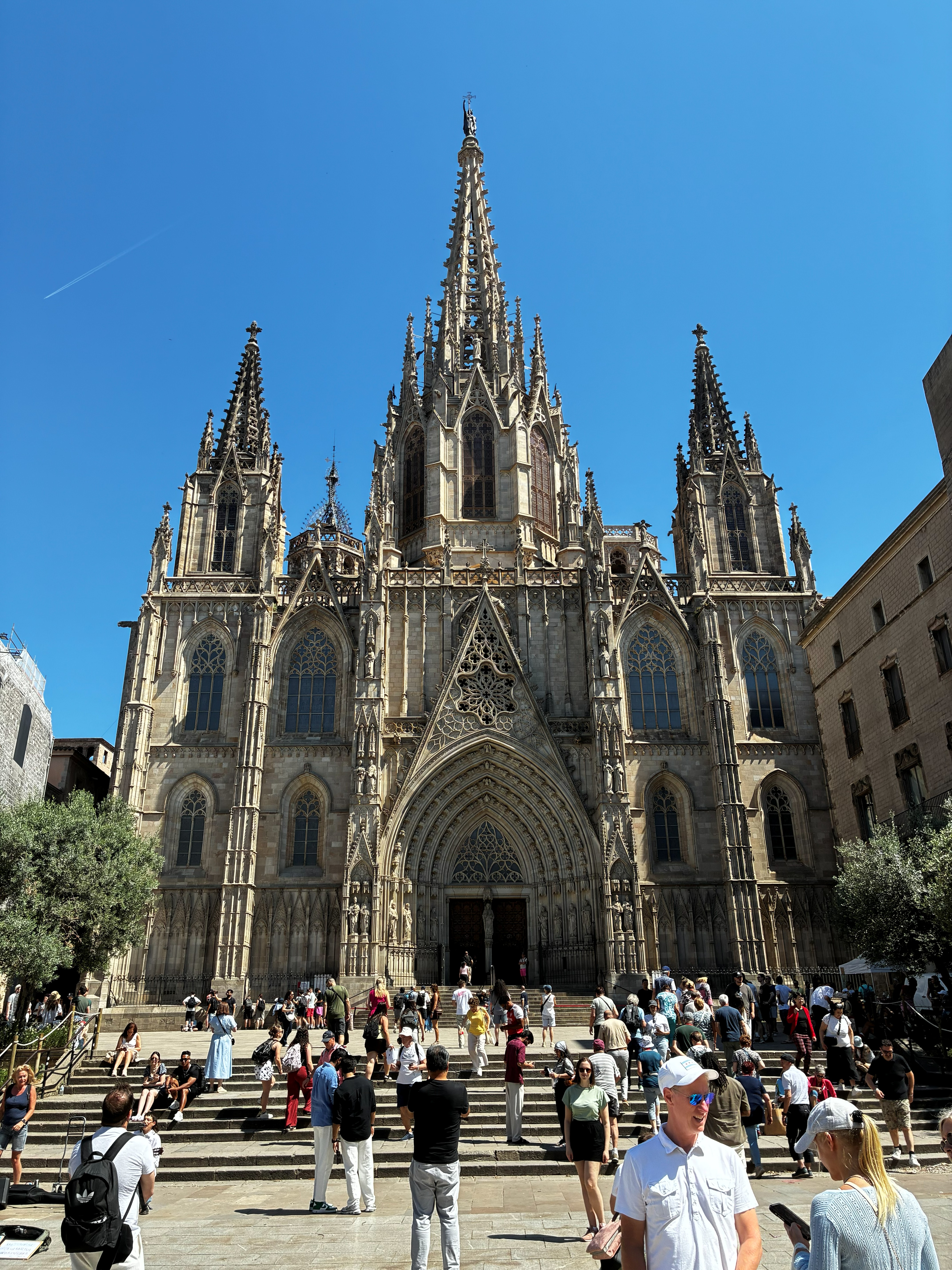 Gothic Barcelona Cathedral (Catedral de la Santa Creu i Santa Eulàlia) facade with spires against a deep blue sky and crowds on the plaza steps