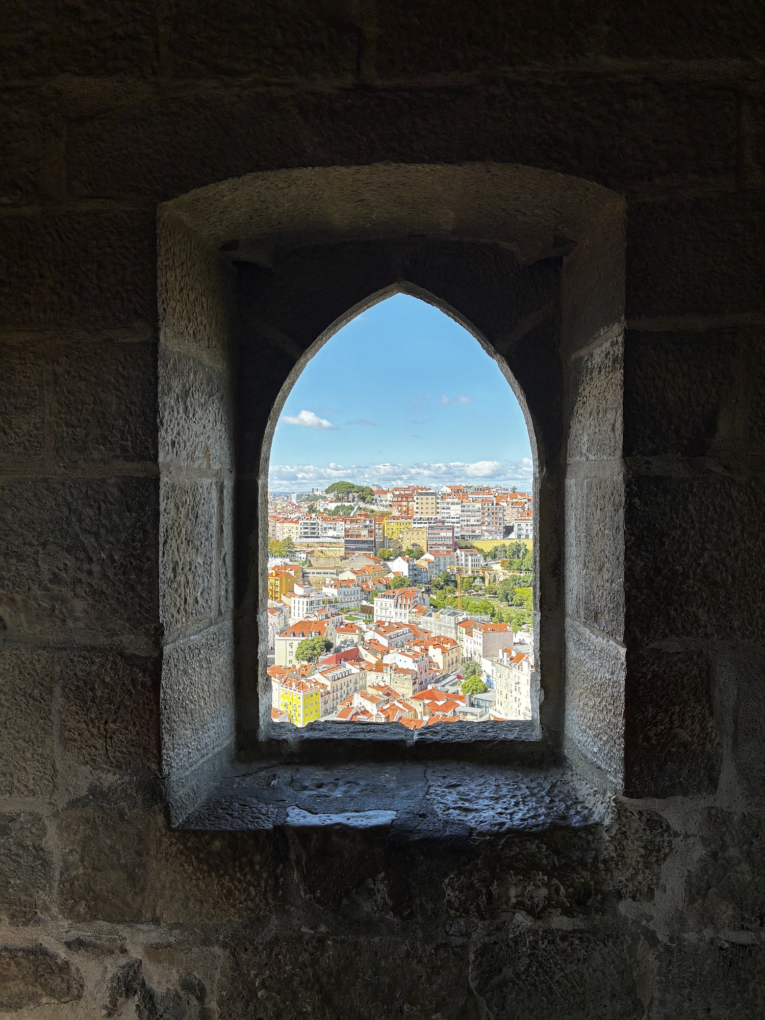 Lisbon's terracotta rooftops and the city skyline framed by a Gothic arched stone window in Castelo de São Jorge