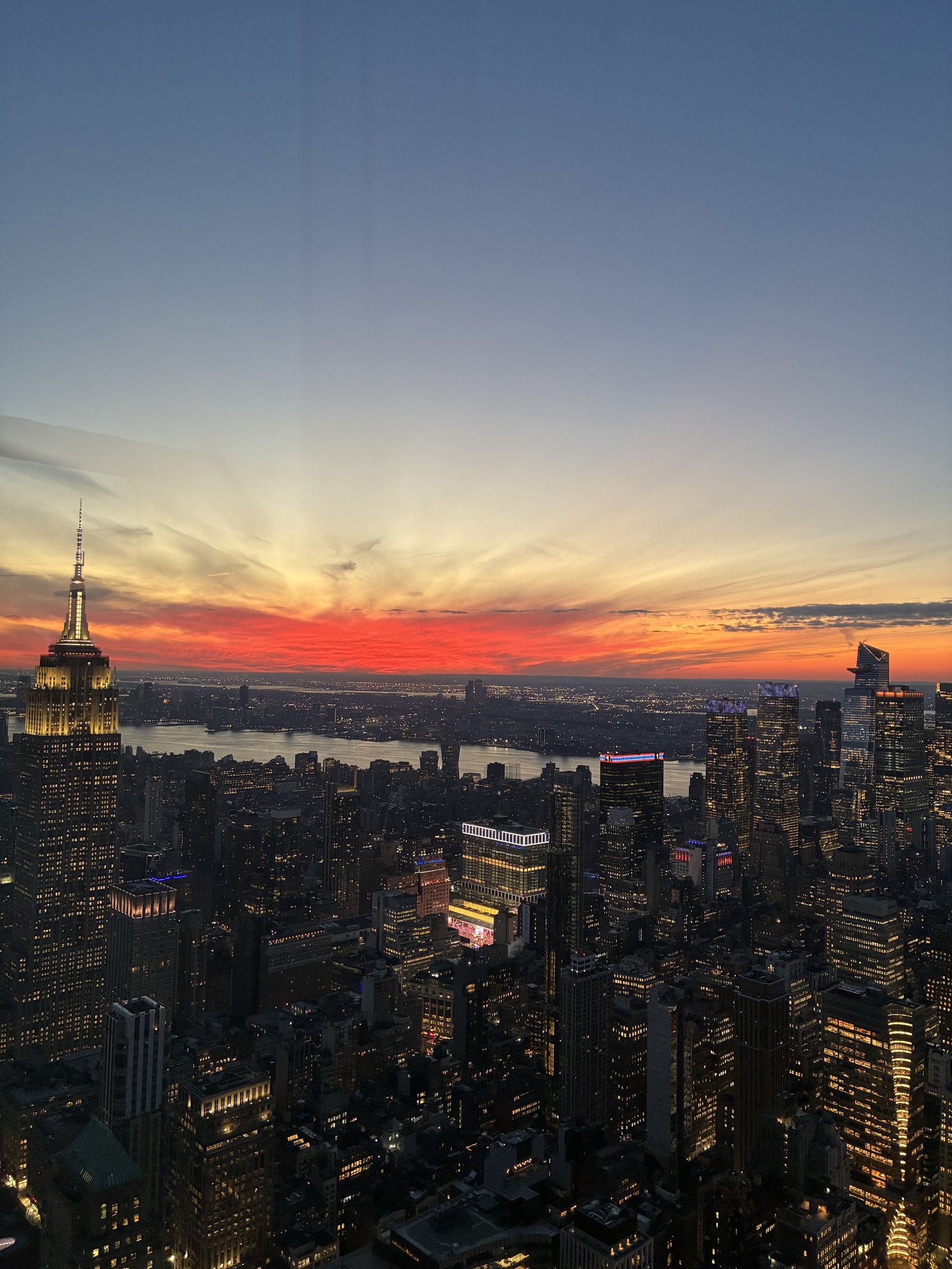 Empire State Building and the Manhattan skyline lit up under a vivid red-orange sunset sky