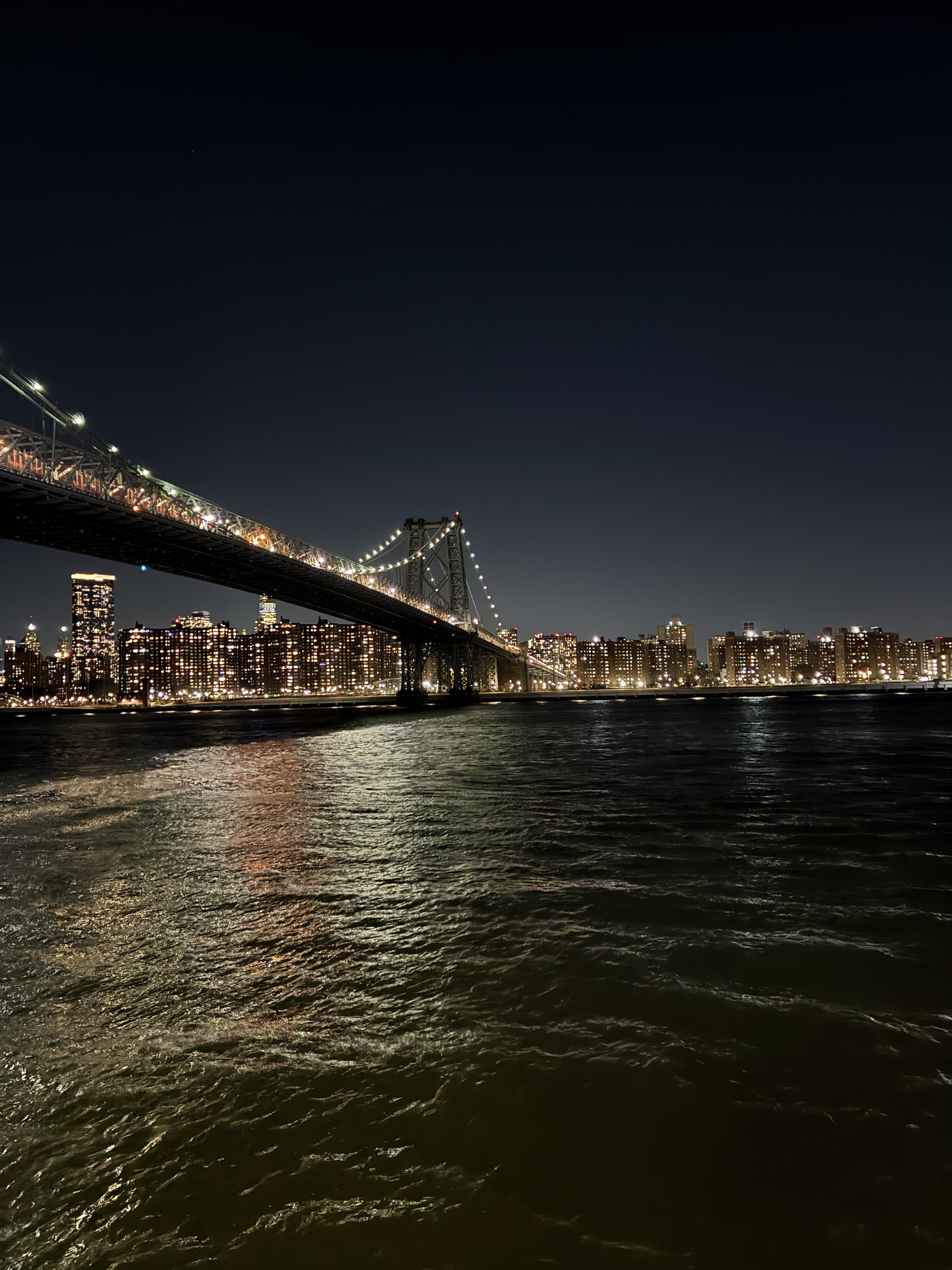 Williamsburg Bridge strung with lights arching over the dark East River at night